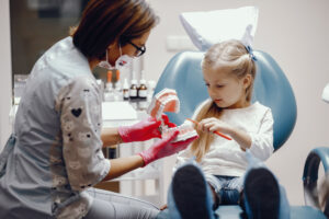 Pediatric Dental Services in Crystal Lake: Complete Care for Growing Smiles 2 Dentist explaining dental tools to a child using a mirror or toy model.