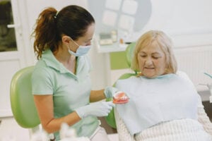 Can Dental Implants Be Removed and Replaced with Dentures? Understanding Your Options 1 Dentist explaining dental implant treatment options to an older patient during a consultation in a dental office.