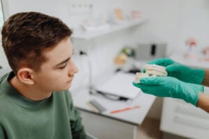 Can Dental Implants Be Removed and Replaced with Dentures? Understanding Your Options 2 Dentist showing a dental model to a patient while discussing tooth replacement options and denture treatments.