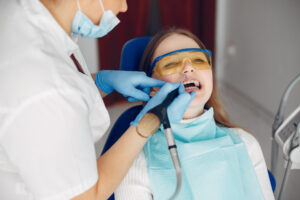 Dental Sealants for Kids in Crystal Lake: Are They Worth It? Cost & Process 2 Child wearing protective glasses during a dental treatment while a dentist uses a suction tool.