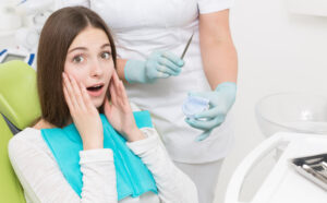 Tooth Extraction in Crystal Lake: What to Expect & How to Recover Fast 1 Young woman holding her cheek while a dentist prepares for an oral examination.