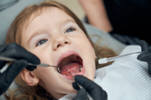Dental Sealants for Kids in Crystal Lake: Are They Worth It? Cost & Process 1 Young child opening her mouth during a dental exam as a dentist uses a mirror and dental tool.