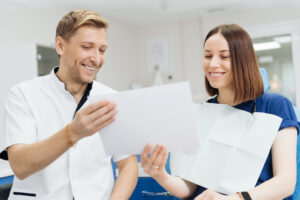 Dental Implants vs Dentures vs Bridges: Which Is Right for You? 2 Dentist and patient smiling while reviewing treatment information in a dental office.
