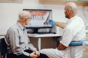 Full Mouth Dental Implants After Dentures: Your Options 2 Dentist explaining dental implant treatment to an older patient using a digital model on a monito