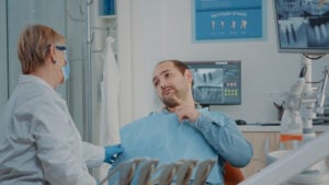 Are Dental Implants Safe Long-Term? An Honest 2026 Answer 2 Male patient pointing to his jaw while discussing dental pain with a dentist.