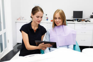 Space Maintainers for Kids: What They Are & When Your Child Needs One 2 Dental professional showing a tablet to a patient wearing a purple bib in a dental clinic.