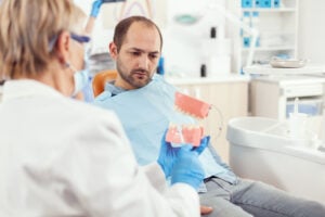 Are Dental Implants Safe Long-Term? An Honest 2026 Answer 1 Dentist explaining proper oral hygiene to a male patient using a dental model.