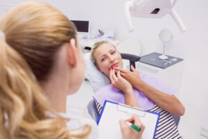 Broken or Chipped Tooth: What to Do Right Away (Same-Day Emergency) 1 Female patient holding her jaw in pain while speaking with a dentist during a consultation.