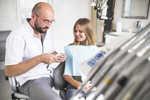 Dental Crowns in Crystal Lake: Types, Cost & What to Expect in 2026 2 Dentist showing a dental model to a smiling female patient during a consultation.
