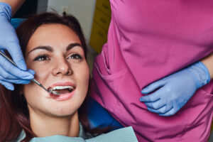 Gum Recession & Dental Implants: Can You Still Get Implants? 2 Female patient undergoing a dental examination with a mirror while seated in a dentist’s chair.