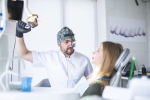 What Is a Prosthodontist? Prosthodontist vs. General Dentist 2 Dentist wearing magnifying loupes preparing to examine a female patient in a dental chair.