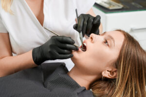 Cracked Tooth? Signs, Treatment Options & When to See a Dentist 2 Dentist examining a female patient’s teeth with dental instruments during a routine checkup.