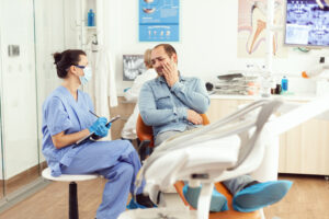 Tooth Pain Relief at Home: What Works & When to Call a Dentist 2 Male dental patient holding his cheek in pain while discussing his symptoms with a dental professional.