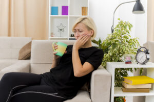 Tooth Pain Relief at Home: What Works & When to Call a Dentist 1 Woman sitting on a sofa holding her cheek in pain